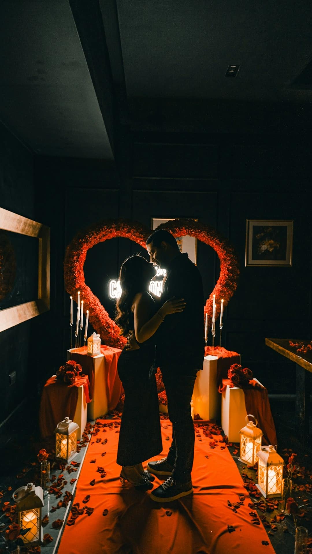 A couple embraces affectionately under a heart-shaped floral arch.