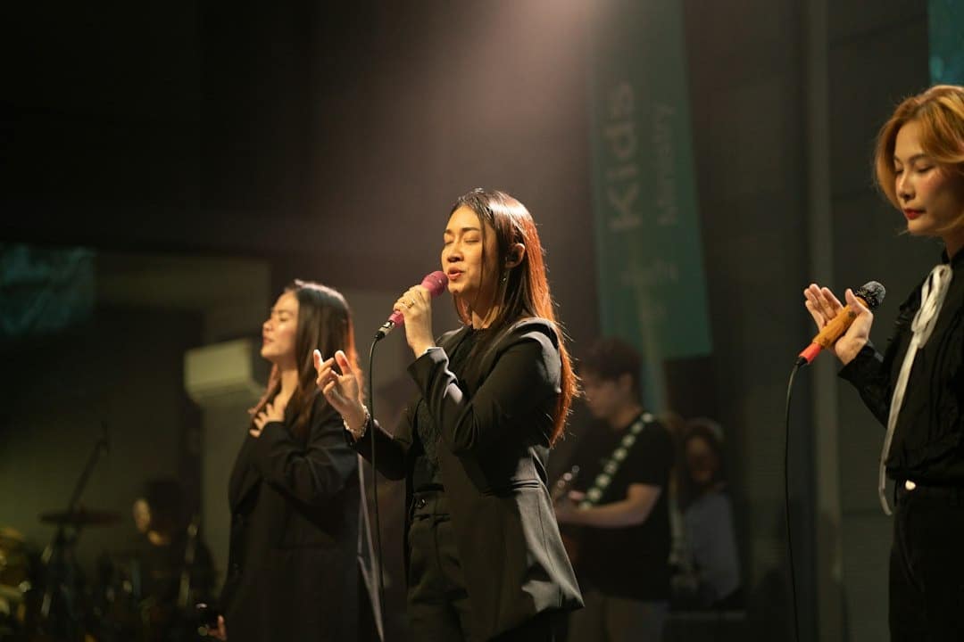 Three women sing emotionally on a stage with warm backlighting.